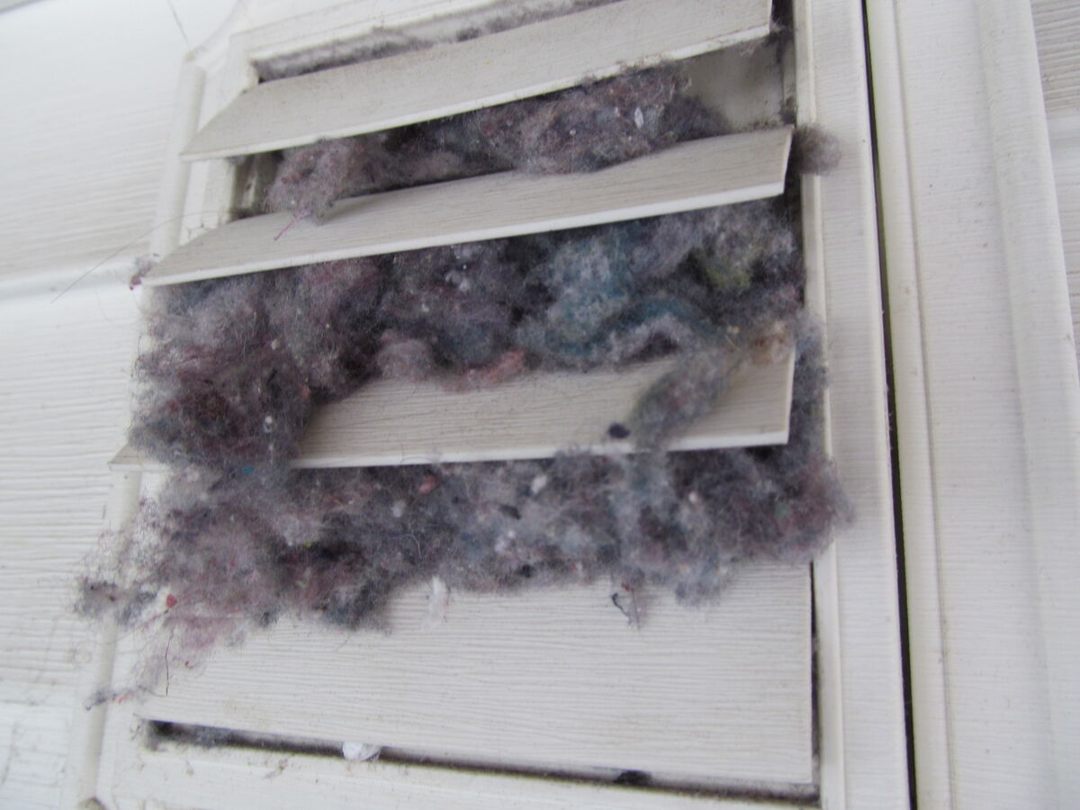 Exterior louvered vent completely clogged with lint on white siding